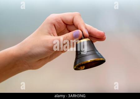 A small bell in the girl's hand on a neutral background, close-up Stock Photo