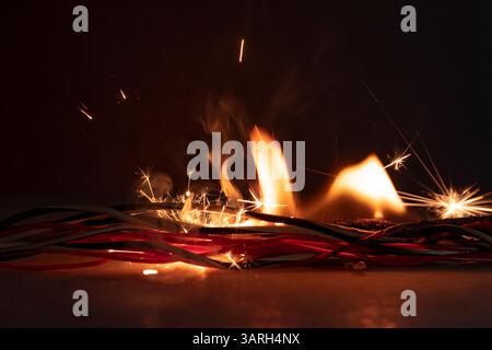 Electric wires are burning on a dark background. A short circuit in the wires., the cause of the fire.Flames, sparks and smoke Stock Photo