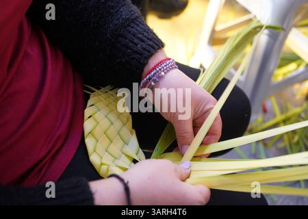Easter custom in Crete, Greece: Woman's hands knitting crosses from palm fronds that are shared on Palm Sunday Stock Photo