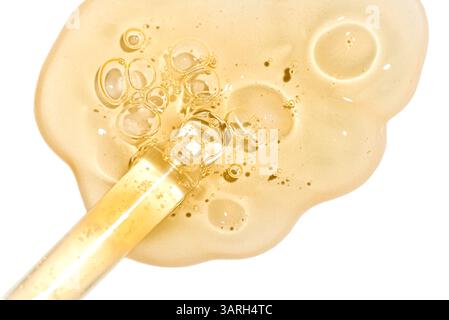 Dropper pipette and sample of golden face serum or retinol gel isolated on white background extremely close up. Skin care with oil or peptide. Texture Stock Photo