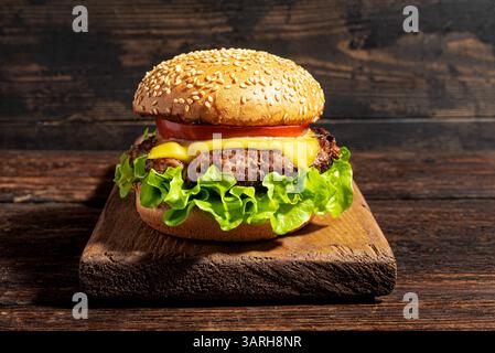 Homemade burger, cheeseburger on dark wooden background. Delicious cheeseburger with american cheese, lettuce, tomato and fresh bun, burger party conc Stock Photo