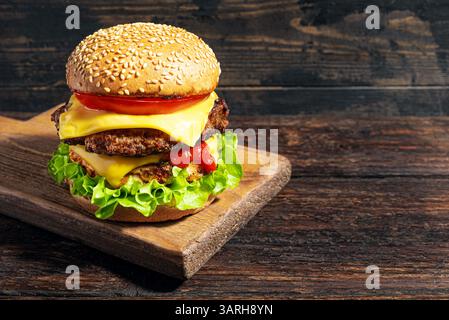 Double cheeseburger with lettuce, tomato, ketchup and melted american cheese on dark wooden background, copy space. Big burger with extra meat. Hambur Stock Photo