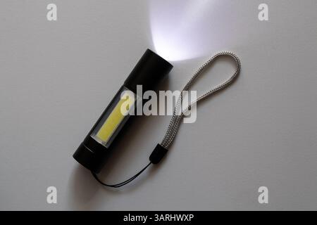 Small pocket portable black flashlight with led lights shines on white background in the dark Stock Photo