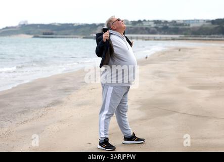 Elderly man embracing the sea breeze with joy on a quiet beach, wearing casual sportswear, sunglasses Stock Photo