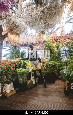 Beautiful young woman wearing short pants, short bomber jacket and high black boots.Fashion model is enjoying the beauty and smell of colorful flowers Stock Photo