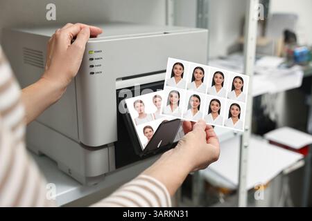 Worker with passport photos of women near modern printer indoors, closeup Stock Photo