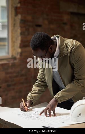 Vertical shot of African American architect leaning over table drawing sketch of future office, he focused on details Stock Photo