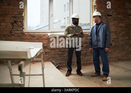 Two biracial builders having conversation while working at construction site together Stock Photo
