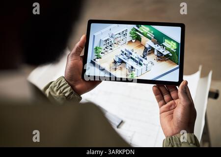 Over shoulder view of unrecognizable foreman holding black tablet with layout plan of IT office on screen Stock Photo