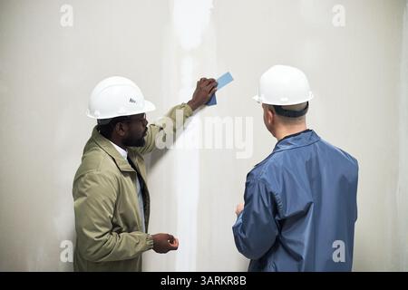 Two male biracial interior designers wearing plastic hardhats while discussing wall color of color palette Stock Photo