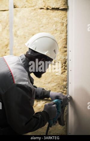 Vertical shot of African American man in uniform and with plastic hardhat on head working at construction site Stock Photo