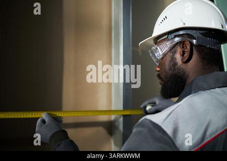 Bearded male worker standing in front of wall and using measure tape and looking at it Stock Photo