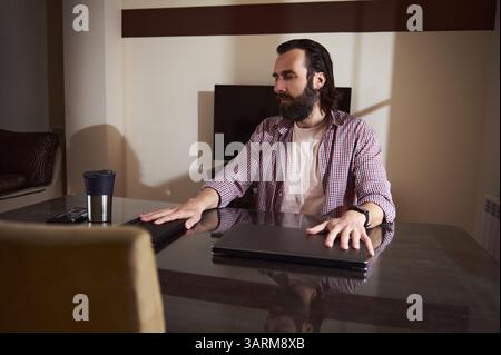 A contemporary workspace featuring a thoughtful young entrepreneur managing tasks and overseeing projects, embracing a digital nomad lifestyle. Stock Photo