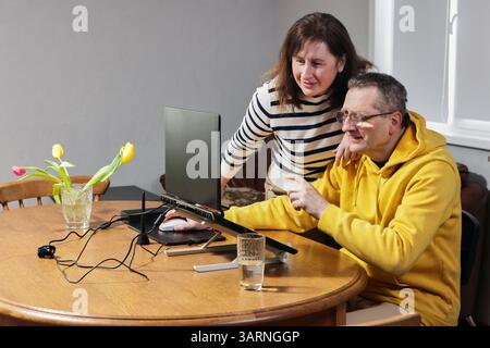 Woman watches man with glasses point at computer monitor placed on wooden desk, intently focused. Stock Photo