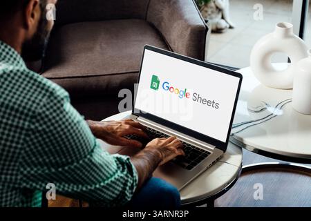 Man using a laptop computer displaying logo of Google Sheets on the screen. Online spreadsheet software for calculate, formulas and productivity. ROSA Stock Photo