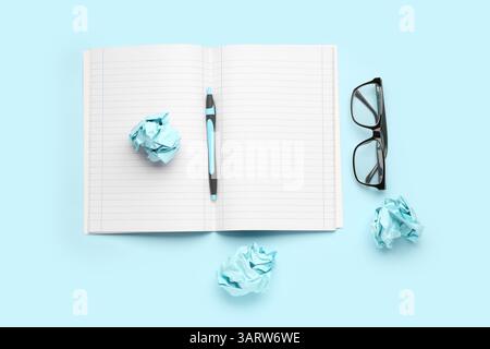 Open notebook, pen, eyeglasses and crumpled paper balls on color background Stock Photo