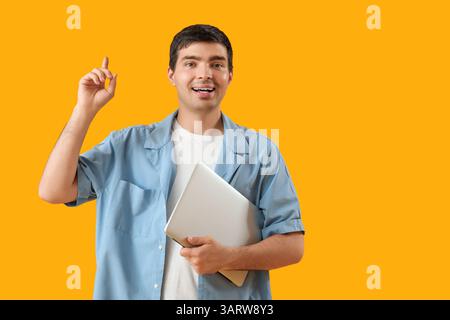 Male programmer with laptop pointing at something on orange background Stock Photo