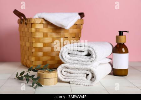 Clean towels, cosmetic products and wicker basket on light tile table against pink background Stock Photo
