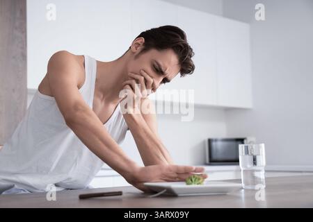 Young man with anorexia refusing from food in kitchen Stock Photo