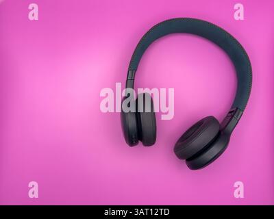 Green earphones with soft earbuds and a soft headband are lying on the right side of the image on a pink background. High quality photo Stock Photo