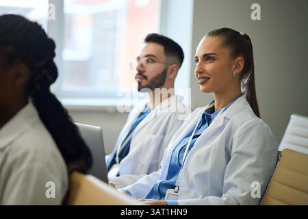 Group of medical students engaged in a classroom lecture, wearing lab coats and taking notes. Bright, professional setting with focused and attentive Stock Photo