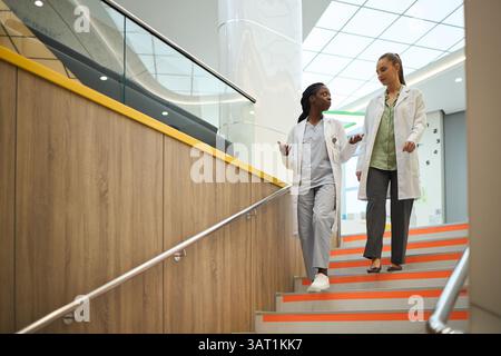 Medical professionals discussing patient care while walking down stairs in modern hospital setting. Healthcare workers collaborating and sharing insig Stock Photo