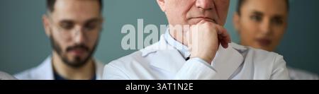 Three medical professionals wearing white lab coats standing together, engaged in a serious discussion regarding patient care and medical procedures Stock Photo