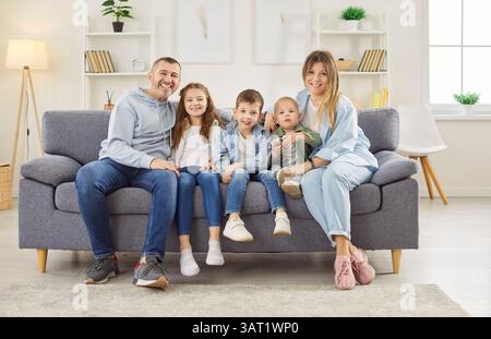Happy family sitting together on gray sofa in living room, smiling and making group photo at home. Stock Photo