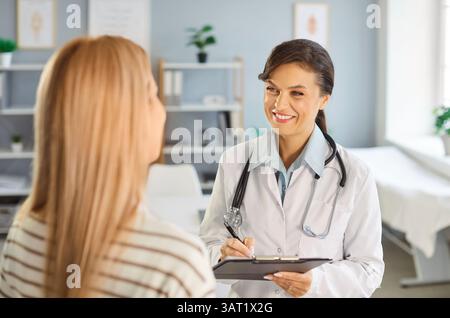 Smiling female doctor consulting young woman patient, taking notes and discussing treatment plan. Stock Photo