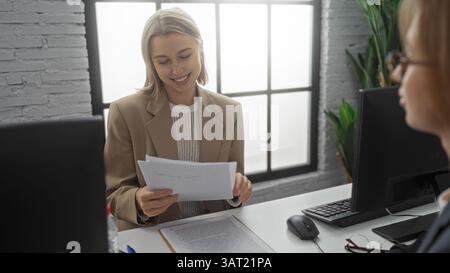 Women executives discussing documents in a modern office environment, showcasing teamwork and professional workplace collaboration indoors with smilin Stock Photo