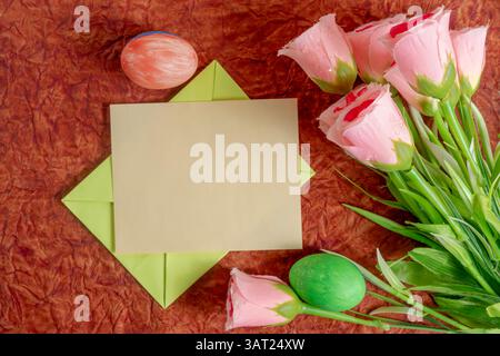 A festive flat lay featuring pink flowers, a blank card, and Easter-themed decorations, perfect for seasonal greetings or creative invitation. Stock Photo