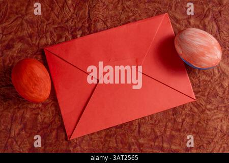 A vibrant red envelope sits on a hard surface with two colorful hand painted eggs. Stock Photo