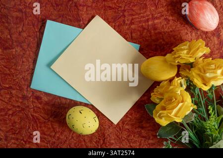 Bright yellow roses, painted Easter eggs and colorful paper placemats create a festive backdrop. Perfect for celebrating the Easter holiday and creati Stock Photo