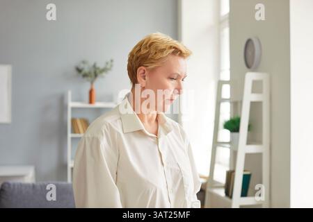 Pensive middle-aged exhausted aged woman alone in living room looking sad thinking pondering Stock Photo
