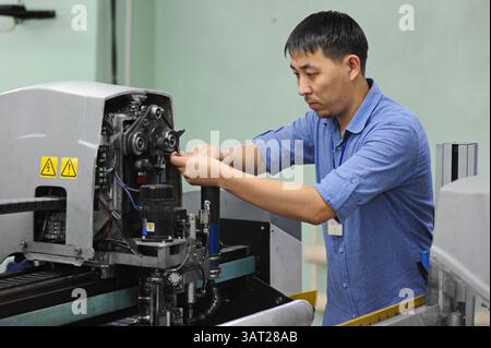 A worker repairs an embroidery machine in a sewing workshop Stock Photo