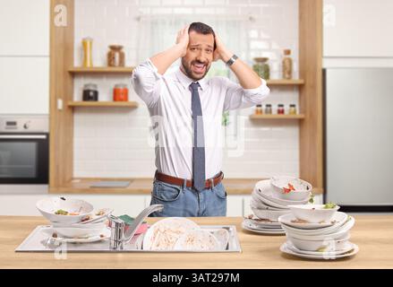 Worried man in a kitchen with a pile of dirty dishes Stock Photo