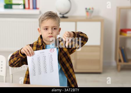 School grade. Sad boy holding answer sheet with letter C and minus symbol indoors, space for text Stock Photo