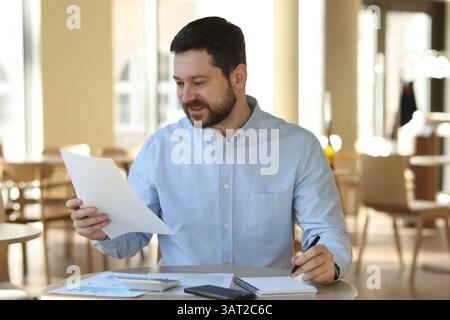 Smiling business owner doing paperwork at table in his cafe Stock Photo