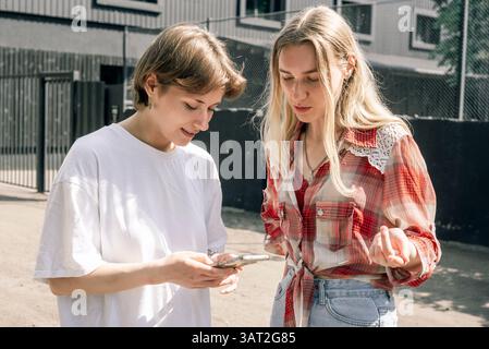 Two young women discussing something on phone outdoors Stock Photo