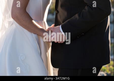 Bride and groom holding hands in sunlight during wedding ceremon Stock Photo