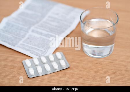 White capsules, glasses of water and a prescription are placed on a table. Stock Photo