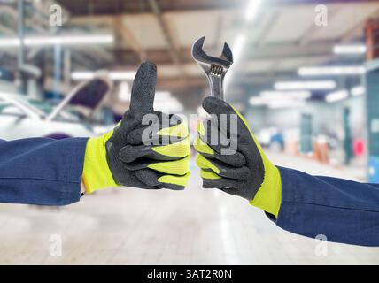 Cropped image of mechanics working in auto service. One is holding a spanner while the other is showing Ok sign at repair shop Stock Photo