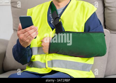 Close up of repairman hands with broken arm wearing sling using smart phone at home Stock Photo
