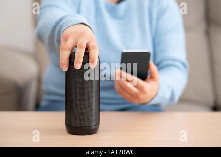 Close-up on female hand using phone connecting speaker at home. Stock Photo
