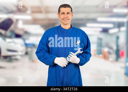 Portrait of confident mature mechanic or blue-collar with wrench and blue overall looking at camera standing in repair shop. Stock Photo