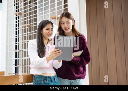 Study Time and Friendship. Two students sharing study materials while bonding over their digital device in a modern school setting. Stock Photo