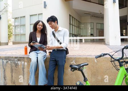Sustainability and Collaboration. Two young professionals discussing eco-friendly initiatives over coffee and digital devices. Stock Photo