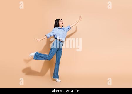 Young businesswoman joyfully posing with an elegant outfit on a minimal beige background, expressing confidence and positivity. Stock Photo