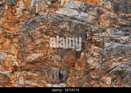 A close-up view of a rocky cliff face showcasing various shades of brown, orange, and black with distinct rock formations and textures Stock Photo