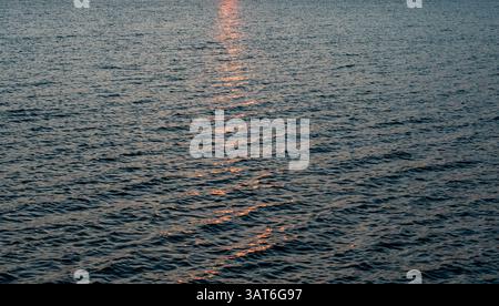 Sunrise reflected in the waves of the Rappahannock River a Wide expanse of water with gentle ripples reflecting a warm, reddish light Stock Photo
